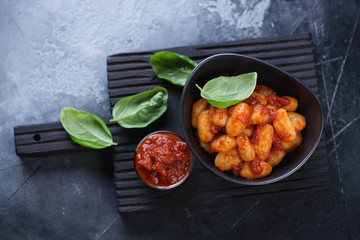 Black wooden serving board with a bowl of potato gnocchi with red pesto sauce, high angle view, horizontal shot