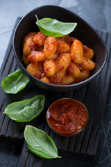 Potato gnocchi served with red pesto and fresh green basil leaves, close-up, studio shot