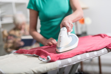 Home helper ironing clothes for an old woman