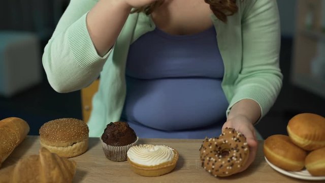 Obese teenager biting muffins and donuts, overeating sweets, unhealthy food