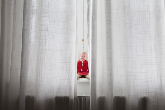 Doll sitting on windowsill behind curtains