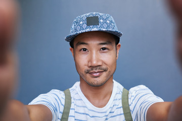 Smiling young Asian man taking a selfie outside