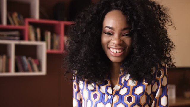 Portrait of a beautiful young afro american woman with curly hair turns her head looking into the camera and smiling in a cafe