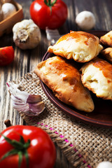 Hearty and tasty food, national Ukrainian cuisine, pies made of yeast dough with mushrooms, tomatoes and spices on rushnyk on a dark rustic wooden background  