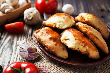 Hearty and tasty food, national Ukrainian cuisine, pies made of yeast dough with mushrooms, tomatoes and spices on rushnyk on a dark rustic wooden background  