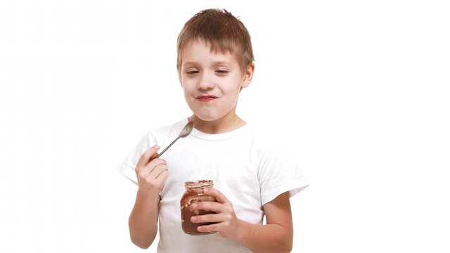 Elementary-school aged Caucasian boy eating chocolate spread with great pleasure standing on white background