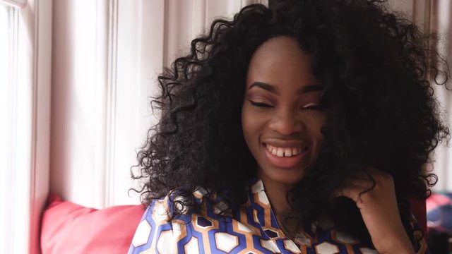 Portrait of a beautiful young afro american woman with curly hair turns her head looking into the camera and smiling in a cafe