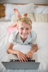 Portrait of smiling boy using laptop on bed in bedroom