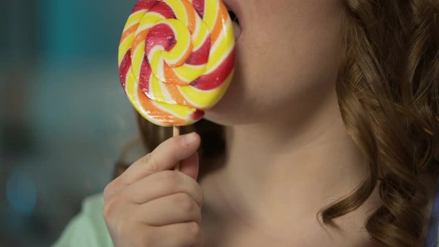 Obese lady licking big colorful lollipop, overeating sugar, risk of diabetes