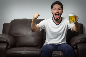 Handsome young man watching TV and cheering while sitting on the sofa at home