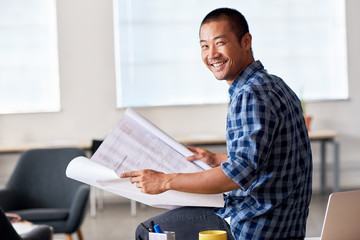 Smiling Asian architect reading blueprints in an office