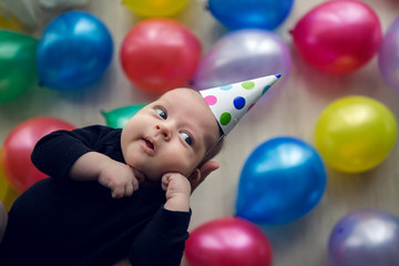 Fototapeta na wymiar child in a festive cap in polka-dot lies on his hands against the background of colorful balloons