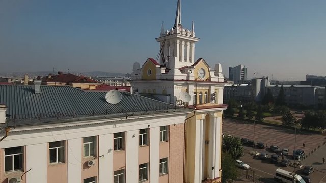 Zabaikalles committee and broadcasting building Soviet Square. Russia Ulan-Ude Siberia. Monument to Lenin on background Road traffic clock roof. Summer. Approach close to the building Flight Aerial 4k