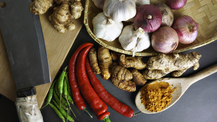 Asian cuisine ingredients of herbs, spices, turmeric, red pepper, green pepper, knife, garlic and shallots. on a black background. View from the Top