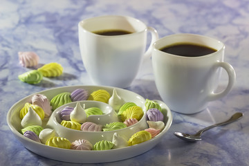 Meringue cake on a white plate and two cups of coffee on a blue marble table.