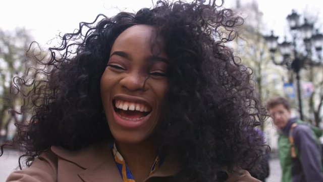 Portrait of a beautiful young afro american woman with curly hair turns the camera smiling, happy feeling in the city center