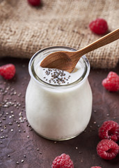 White yogurt with raspberries in glass bowl on rustic table.