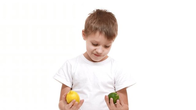 Elementary-school aged Caucasian boy standing on white background and holding lemon and lime in hands. Than drawing lemon to camera