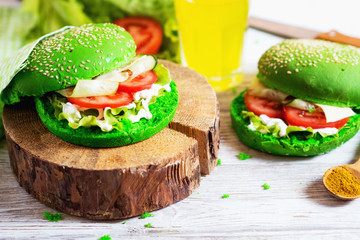 Fast food, barbecue, vegetarian burger with a green bun with sesame, fresh cucumber, tomato, lettuce, cheese mayonnaise and spices, with a glass of juice on a white rustic wooden background
