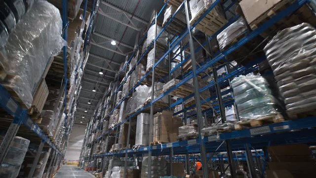 Camera moving between palettes with ordered goods and materials at warehouse. Large warehouse logistics terminal. Multi level storage with racks full of goods and materials
