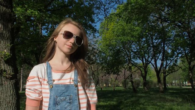 Girl in sunglasses in the park. Girl teenager with freckles close-up. Teenager on a sunny day in the fresh air. Slow motion.