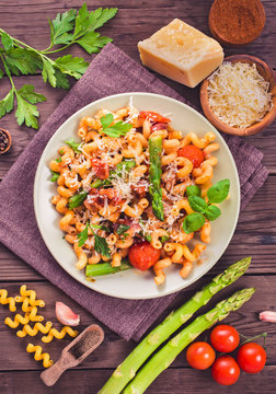 Italian cavatappi pasta with asparagus and tomatoes on wooden table, top view, toned