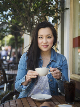 Smiling Chinese woman drinking coffee at outdoor cafe