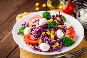 Fresh vegetable salad with mozzarella on wooden table.