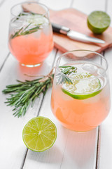 glass of fresh juice with lime, rosemary and knife on wooden background
