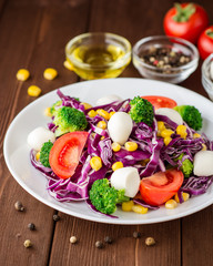 Fresh vegetable salad with mozzarella on wooden table.