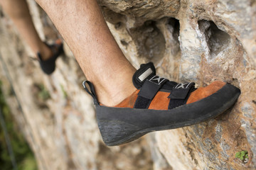 Rock climber about to start climbing his route, bottom view with his foot on the foreground - Powered by Adobe