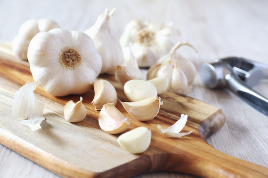 Bulbs of garlic on cutting board and garlic press