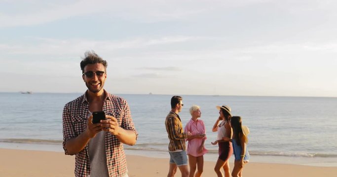 Latin Guy Use Cell Smart Phone Welcome People Group To Take Selfie Photo On Beach, Happy Smiling Man And Woman Friends Slow Motion 60
