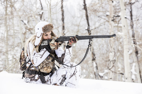 Caucasian woman hunting in forest aiming rifle