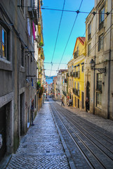 Steep narrow street of Lisbon with cable car rails in the middle and ocean in the background