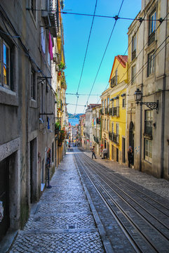 Steep narrow street of Lisbon with cable car rails in the middle and ocean in the background