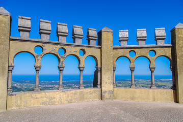 Castle balcony with arched portals and panoramic view of forests and ocean in the background