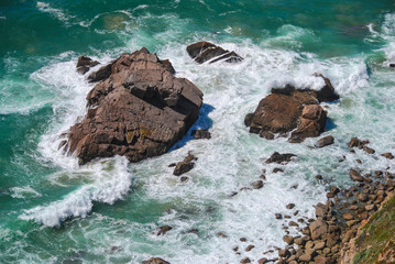 Aerial view of green sea water with waves smashing on the rocky coast