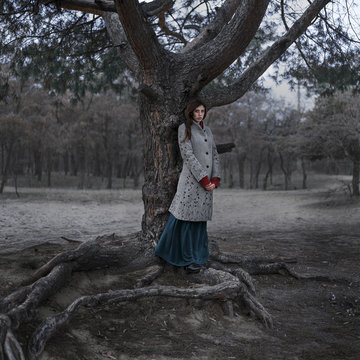 Pensive Caucasian woman standing on root under tree