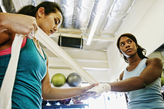 Woman wrapping hands of friend in gymnasium
