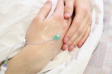 Fototapeta premium Closeup of patients hands in a hospital bed with an IV 