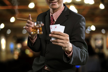 Handsome man holding glass of whiskey with cigarette and show winning in poker games.