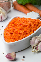 Carrot salad. French Grated Carrot Salad. Shredded carrot with garlic, basil and black pepper on the white rustic background. Vegan food. Vegetarian menu. Spring menu.