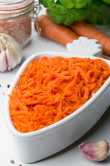 Carrot salad. French Grated Carrot Salad. Shredded carrot with garlic, basil and black pepper on the white rustic background. Vegan food. Vegetarian menu. Spring menu.