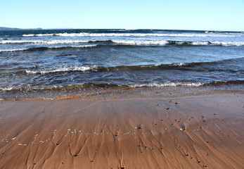 Beach background scene with clear blue sky and waves rolling on the beach. White foam on beach, water nature. Summertime, blue sea and waves and yellow sand.