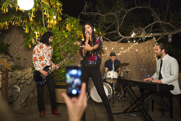 Person using cell phone recording band performing music on stage