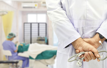 Doctor in a white gown holds the stethoscope on blur operating room background.