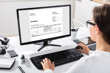 Businesswoman Calculating Invoice On Computer