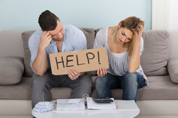 Worried Couple Holding Help Sign While Calculating Bills