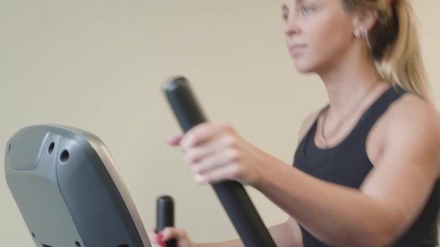 pretty 20s woman in sportswear in working on ellipsoid machine in a gym